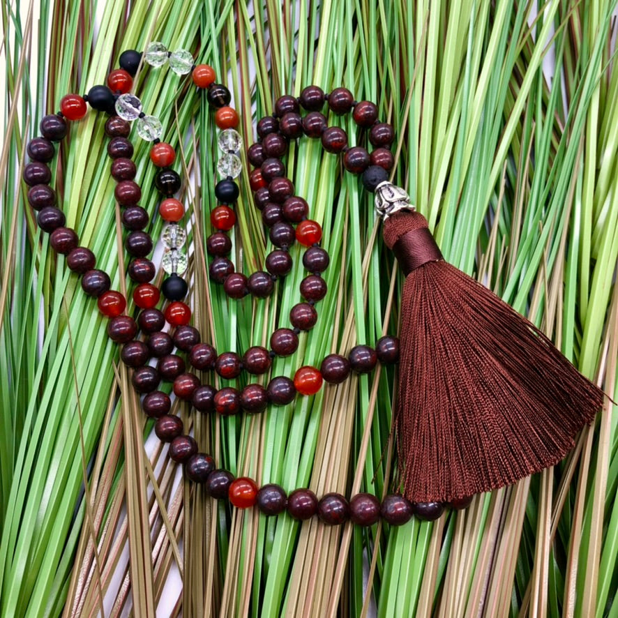 Red jasper necklace with burgundy tassel on top of grass