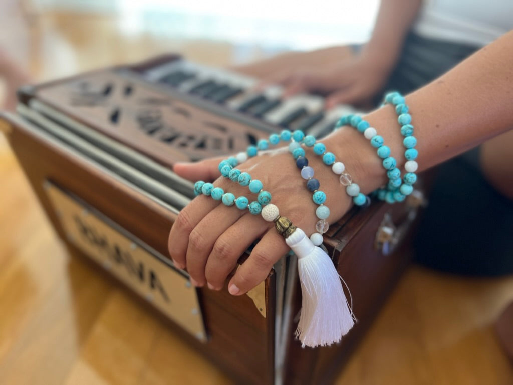 women playing harmonium with turquoise mala necklace with white tassel