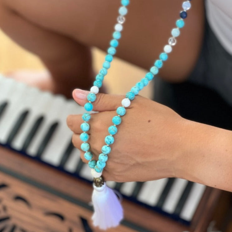 Women holding turquoise stone necklace with white tassel 