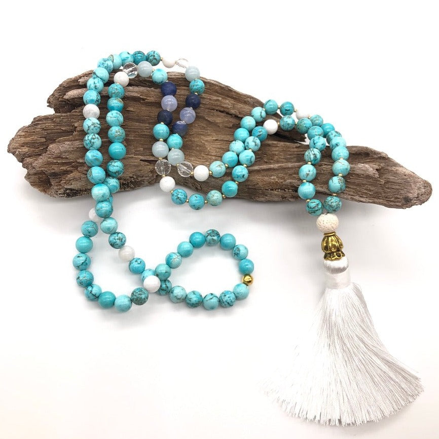 turquoise stone necklace with gold cone and white tassel on top of wood