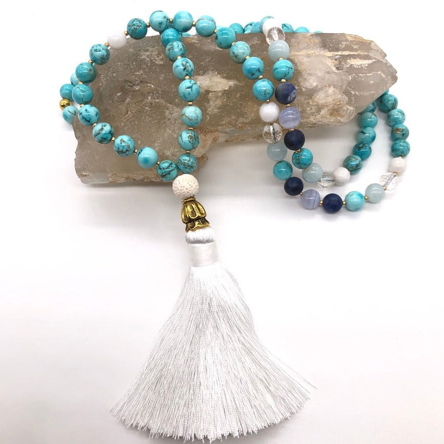 turquoise stone necklace with gold cone and white tassel sits on top of smokey quartz